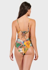 Flerfärgad baddräkt med låg rygg och knytdetalj. Har livliga abstrakta mönster i gröna, orangea och blå nyanser.