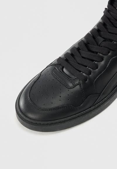 Adidași din piele neagră cu bot deține perforații, șireturi rotunde și talpă din cauciuc texturat negru. Prezintă un design elegant și accente de cusătură subtile.