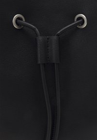 Černá kožená taška se zaměřením na texturovaný povrch, dvě kovové očka a stahovací šňůrku s koženým uzávěrem.