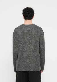 Γκρι μπλούζα με μακριά μανίκια, που φέρει λεπτό μοτίβο λεοπάρδαλης, στρογγυλή λαιμόκοψη και άνετη εφαρμογή, συνδυασμένη με σκούρο φαρδύ παντελόνι.