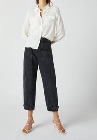 Biała, długa koszula z guzikami i dwoma kieszeniami na piersi, w połączeniu z czarnymi dżinsami z wysokim stanem. Stylowe beżowe szpilki dopełniają strój.