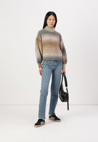 Maglione texturizzato con tonalità gradiente dal marrone al grigio, colletto alto e maniche a sbuffo. Abbinato a jeans blu e sneakers nere. Inclusa una borsa nera.