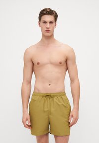 Shorts de bain vert olive avec taille élastique, cordon de serrage et poches latérales. Présente le logo "Calvin Klein" dans une couleur contrastante sur le côté.