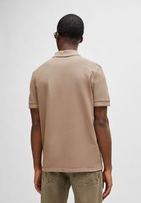 Beige poloshirt met korte mouwen en een kraag, gemaakt van soepel materiaal. Draagt het met gestructureerde groene broek, met simpele lijnen en zonder patronen.