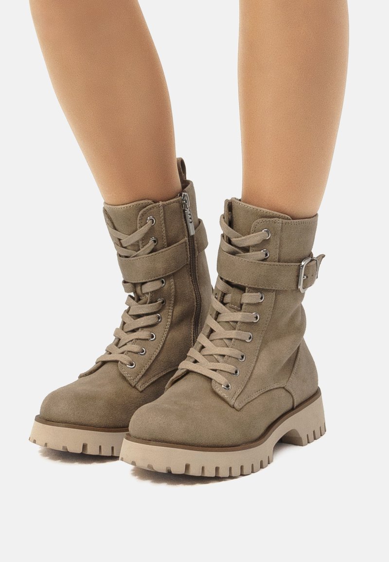 Botas de tobillo de ante verde oliva con cordones en la parte delantera, cremallera lateral y una correa con hebilla. Suela de goma gruesa con textura para un buen agarre.