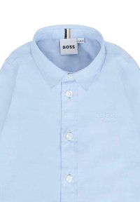 Camicia button-up azzurra chiara in cotone. Presenta un colletto classico, bottoni bianchi e un logo ricamato "BOSS". Texture liscia.