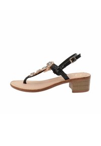 Sandal in pelle nera con tacco basso a blocco, caratterizzato da strass decorativi e design a t-strap. Soletta beige e cinturino alla caviglia regolabile.