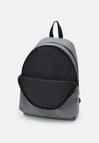Šedý látkový batoh s zaoblenou černou přední kapsou, zipovým uzávěrem a horním uchem. Má hladkou texturu a minimalistický design.