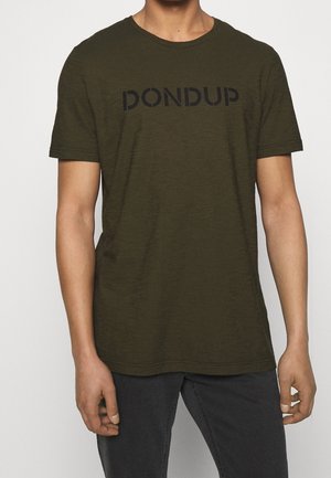 Hombre vestido con una camiseta de manga corta de color verde oliva oscuro con el texto "DONDUP" en negro y jeans gris oscuro, de pie contra un fondo claro y liso.