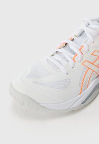 White athletic shoe with mesh upper, orange accents, textured sole, and contrasting laces. Features a rounded toe and padded collar.