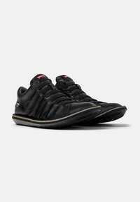Sneakers in pelle nera con tomaia testurizzata, caratterizzati da una punta arrotondata, lacci elastici e una suola resistente con bordo bianco. Logo del marchio rosso sulla linguetta.