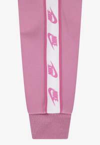 Rosa joggebukser med en hvit stripe og gjentatte rosa "Nike"-logoer. Laget av mykt stoff med ribbestrikkede mansjetter for en tettsittende passform.