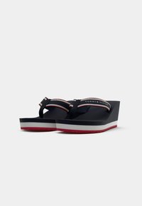 Navy wedge flip-flops with a wide strap featuring a red, white, and blue logo. Textured sole with a contrasting white and red outsole.