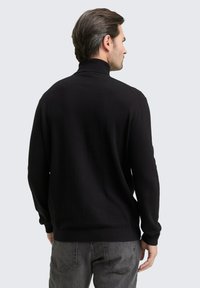 Schwarzer Rollkragenpullover aus einem glatten Strickstoff, mit langen Ärmeln und einer figurbetonten Silhouette. Dezente Rippakzente an den Bündchen und am Saum.