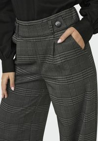 Plaid, high-waisted trousers in gray with black accents. Features a button closure, two side pockets, and a tailored fit.