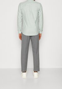 Jasnozielona koszula z długim rękawem i tylnym karczkiem, w połączeniu z szarymi, dopasowanymi spodniami i białymi trampkami, widziana od tyłu.