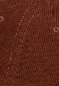 Tissu en velours côtelé marron avec une texture côtelée, présentant des coutures visibles et des accents de couleur foncée ressemblant à des boutons.