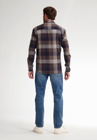 Camicia in flanella a scacchi blu, marrone e grigio con colletto button-down. Presenta maniche lunghe e un orlo curvo, abbinata a jeans blu.