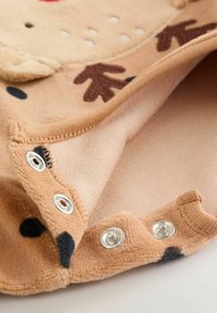 Beige Babybekleidung mit plüschiger Textur, ausgestattet mit Druckknöpfen und dekorativen braunen Geweihen sowie schwarzen Punktakzenten.