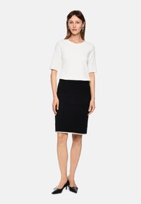 White short-sleeve top paired with a black textured pencil skirt featuring a decorative hem. Model wears black pointed-toe heels.