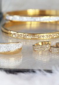 Ensemble de bijoux en or comprenant une bague, des boucles d'oreilles et des bracelets ornés de strass clairs pavés, de surfaces lisses et d'une finition polie.