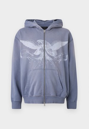 Kapucnis, cipzáros pulóver fakó kék anyagból, melyet grafikusan ábrázolt sas díszít, elülső zsebekkel, bordázott mandzsettákkal és szegéllyel.