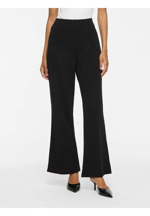 Femme portant un pantalon noir taille haute à jambes larges avec coutures avant, associé à des chaussures noires à talons et bouts pointus.