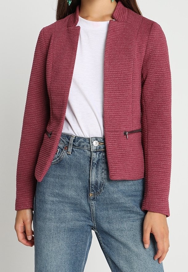 Texturerad bordeauxjacka med krage, utrustad med två sidofickor med dragkedja, kombinerad med en vit t-shirt och blå denimjeans.