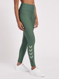 Hooggewaisted groene legging gemaakt van gladde stof, met een zigzagpatroon in een lichter groen op het linkerbeen en een klein zwart accent.
