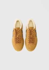 Adidași din suede maro cu o căptușeală pufoasă, șireturi maro și accente negre, având un vârf rotund și un talpă texturată.