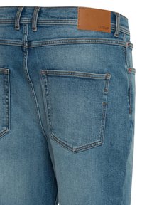 Lyseblå denimjeans med glatt tekstur, med to baklommer, kontrasterende oransje sømmer og en lysebrun skinnetikett på linningen.