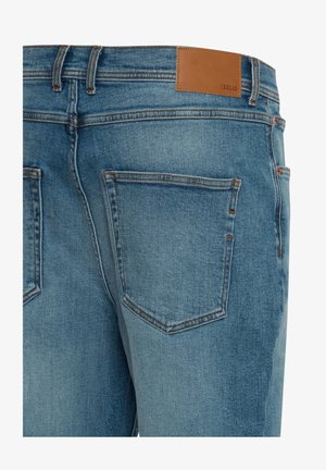 Hellblaue Jeans aus Denim mit glatter Textur, die zwei Gesäßtaschen, kontrastierende orangefarbene Nähte und ein braunes Lederetikett am Bund aufweisen.