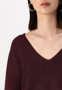 Bordeaux gebreide trui met een V-hals, voorzien van een geribbelde textuur en korte mouwen, aangevuld met metallic accenten in de stof.