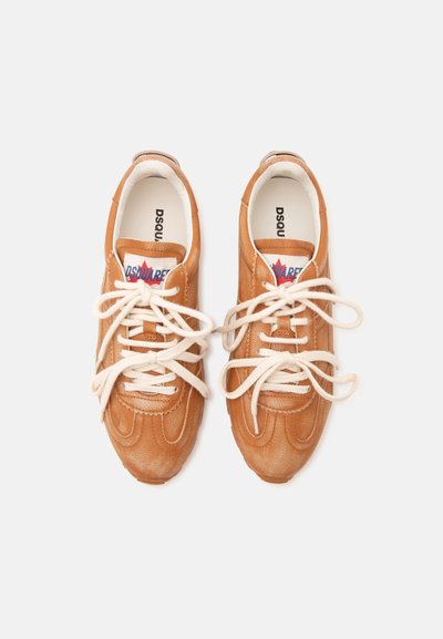 Paire de baskets en cuir marron avec des lacets blancs noués lâchement, nom de la marque visible sur la languette et à l’intérieur de la semelle sur fond blanc.