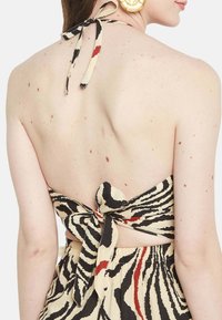 Brezrokavni obleka s trakom na hrbtu, ki ima bež tkanino z črnimi in rdečimi zebra črtami, teksturiran material in odprt hrbet.