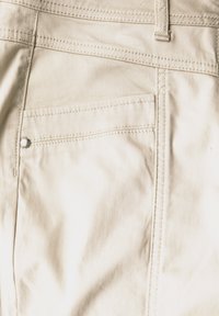 Pantalones de tela beige que presentan un bolsillo trasero con un botón plateado, detalles de costura finos y una textura suave.