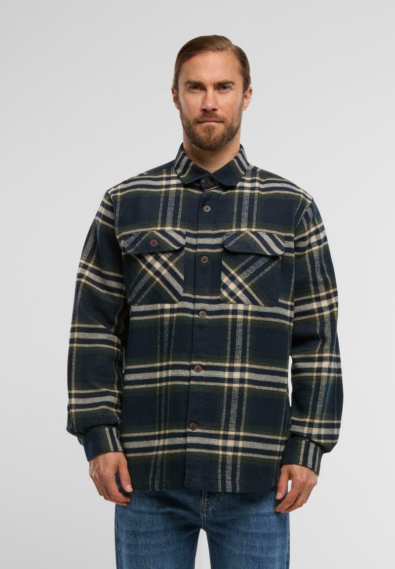 Granatowa koszula flanelowa w kratę z beżowymi i zielonymi paskami, zapinana na guziki z przodu, z dwiema kieszeniami na piersi. Długie rękawy z mankietami na guziki.