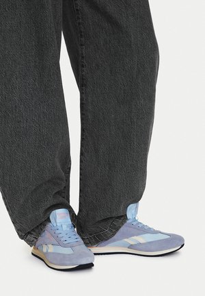 Zapatillas deportivas azul claro con materiales de ante y malla, con rayas y cordones blancos, combinadas con pantalones vaqueros negros holgados.