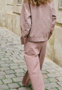 Giacca di cotone rosa con spalle basse e pantaloni a gamba larga coordinati con tasche a toppa, mostrati su una strada lastricata.