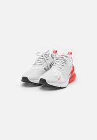 Nike sportcipő, fehér hálós felsőrésszel, piros kiegészítőkkel, kerek orral és fekete gumitalppal, amelyen látható a légpárnázás.