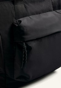 Czarny plecak z nylonu z przednią kieszenią na zamek, teksturowanym materiałem oraz regulowanym zaciągiem z czarnymi detalami.