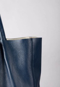 Navy leather tote bag with a textured finish, open top, and long handles. Features visible stitching along the seams.