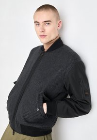 Musthave bomber-jakk, millel on tekstureeritud halli triibulise keha, soonikutega mansetid, tõmblukkudega küljetasku ja tõmblukuga eesmine sulgemine.