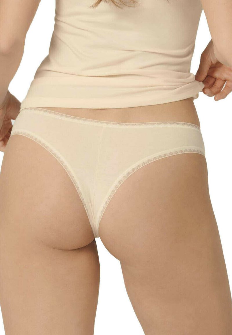 Nudefarbene nahtlose Stringunterwäsche mit Spitzenbesatz, die ein niedrig sitzendes Design und weichen Stoff aufweist, von hinten präsentiert mit glatten Konturen.