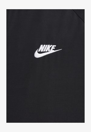 Sort atletisk top med et hvidt broderet Nike-logo på brystet. Stoffet er glat med en subtil tekstur.