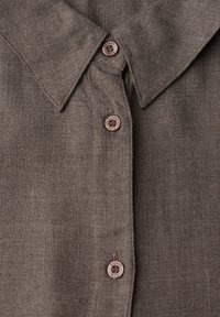 Chemise en lin marron avec un col classique et deux boutons, dont un avec logo. Le tissu a un tissage texturé.