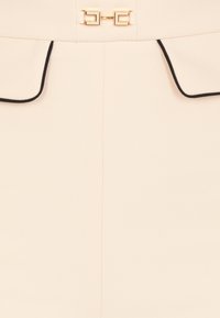 Gonna beige su misura con piping nero. Presenta una chiusura a morsetto dorato in vita, che conferisce struttura a un tessuto morbido e testurizzato.