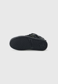 Suela de zapatilla negra con un diseño de goma texturizada y un patrón de rejilla, detalle del logo y bordes reforzados para mayor durabilidad.