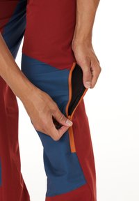 Punisher punas ja siniset ulkopantsit oranssilla vetoketjupussilla, joissa on teksturoitu kangas ja kapea istuvuus nilkoissa.