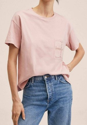 Person iført en lyserød T-shirt med korte ærmer og en tekstureret forlomme, kombineret med højtaljede blå denimjeans.